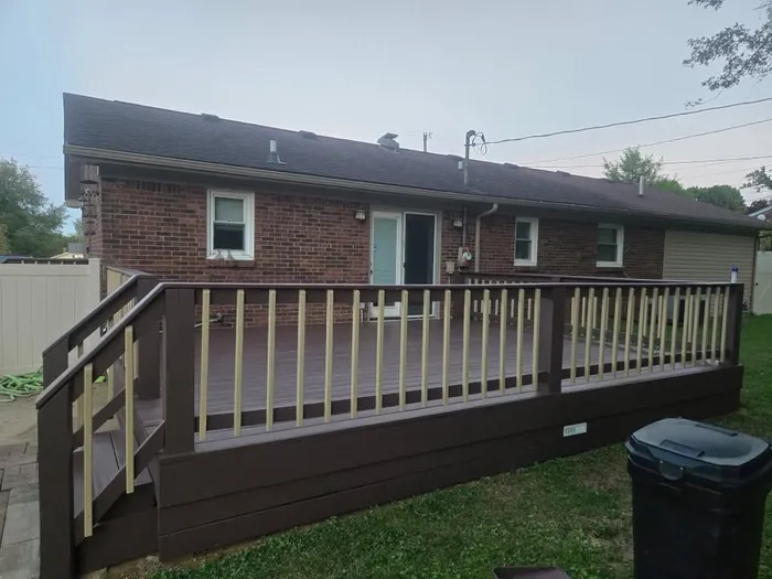Two-tone deck with dark brown floor and light rails behind a brick home
